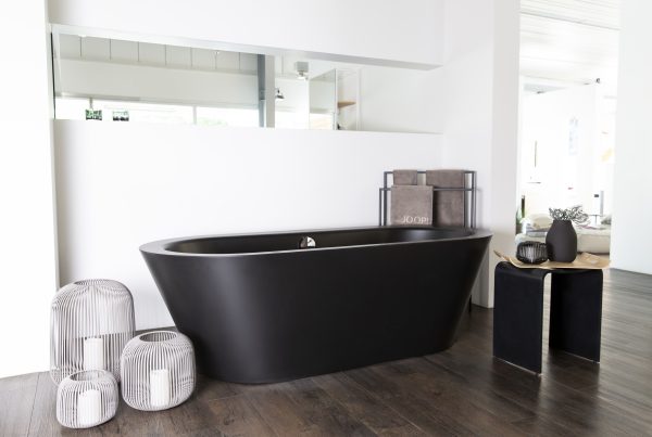 Schwarze Badewanne vor einer weißen Wand mit weißen Accessoires